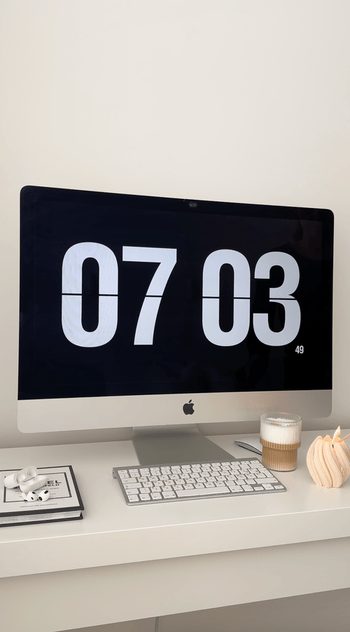 Desktop computer showing a large clock on a tidy white desk