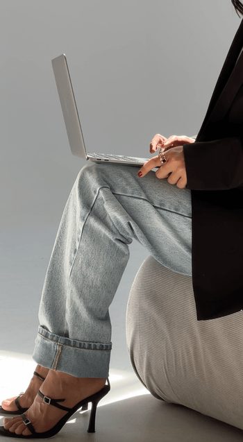 Person in jeans and heels balancing a laptop on their knee