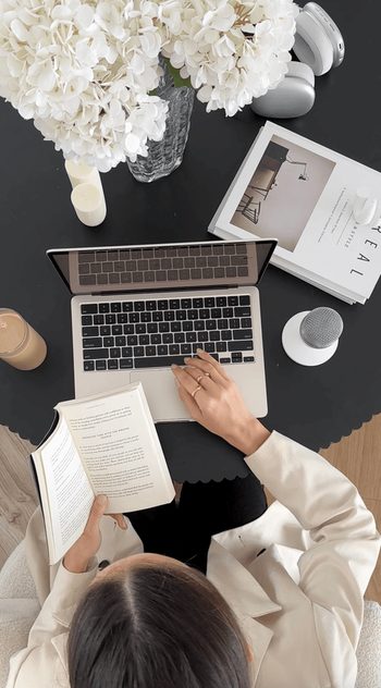 Overhead view of a person reading at a dark desk with a laptop and flowers